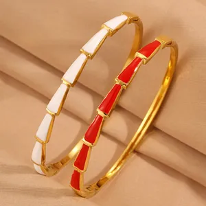 Primo piano di bracciali stile bambù dorati con segmenti in smalto bianco e rosso.