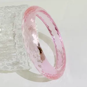 Nahaufnahme eines rosafarbenen Harzarmreifens mit facettiertem Wassergitter-Design