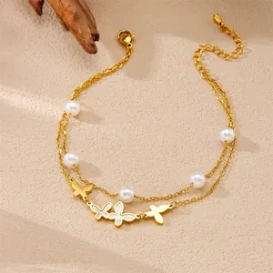 Close-up detail of a double-layered gold anklet with white pearls and butterfly charms