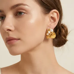 Detailed view of elegant gold heart-shaped earrings with pearl accents on model