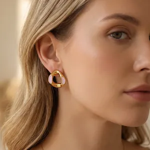 Detailed close-up of geometric gold earrings with pink enamel inlay on a model's ear