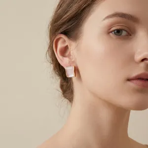 Detailed view of elegant gold-toned square shell stud earrings worn on a model's ear