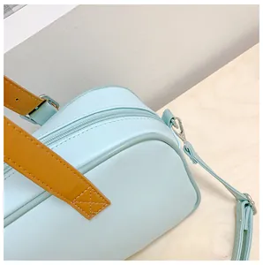 Détail du sac bandoulière bleu clair avec poignées brunes et fermeture éclair en métal