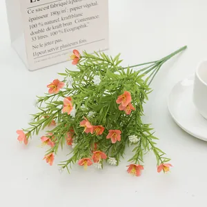 Close-up of artificial orange jasmine bundle with green leaves in a white vase