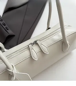 Close-up of minimalist cream leather baguette bag with dual silver zippers and slim handles