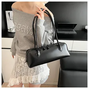 Close-up of a black glossy baguette bag worn by a model in a professional office setting