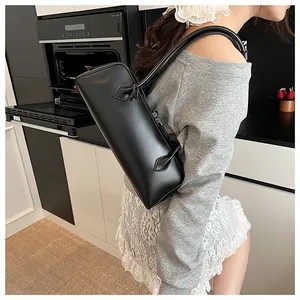 Detail of minimalist black leather baguette bag with long straps on a model in a kitchen