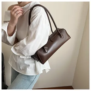 Deep brown long baguette bag shown on shoulder with minimalist white shirt and cream wall