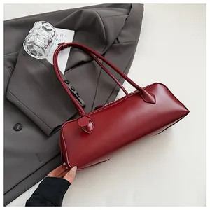 Detailed top view of a dark red glossy leather baguette bag on a grey suit jacket