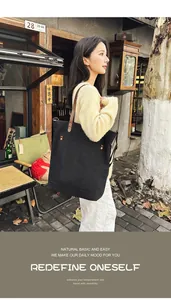 Woman carrying a black canvas tote bag with brown leather straps in a street setting.