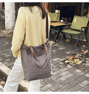 Woman wearing a yellow sweater carrying a large grey canvas tote bag in a street cafe