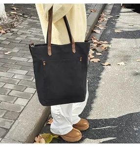 Large black canvas tote bag with brown leather straps shown in an outdoor setting