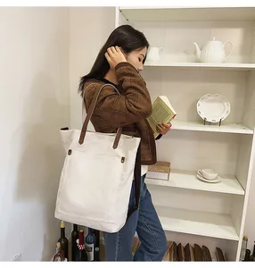 Asian woman carrying a large white canvas tote bag with brown straps in a room