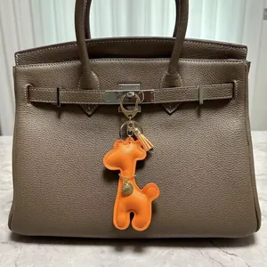 Detailed close-up of a cute orange leather giraffe charm hanging on a luxury handbag