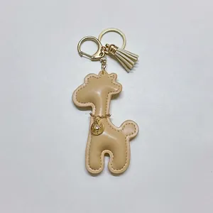 Detailed view of a cute tan faux leather giraffe keychain with a gold tassel and charm