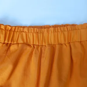Detailed close-up showing the elastic paperbag waistband of orange casual shorts