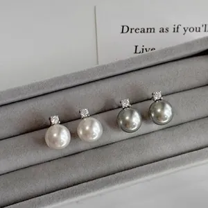 Close-up detail of white and grey pearl stud earrings displayed in a grey jewelry box