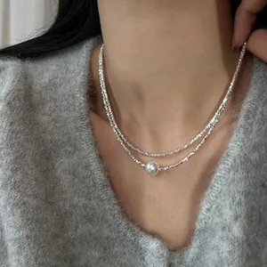 Close-up of double-layered silver necklace with pearl on soft grey sweater