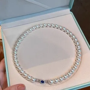 Close-up of an elegant pearl necklace featuring a blue gemstone clasp in a gift box