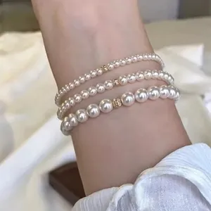 Detailed view of three white pearl bracelets with gold accents on a model's wrist