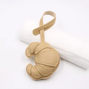 Detailed view of a caramel leather croissant charm featuring delicate white stitching