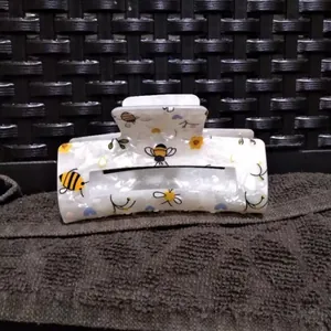 Detail view of a white acrylic hair claw clip with cute bee and flower patterns.