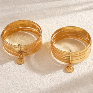 Detail of vintage gold alloy bangle set featuring ethnic patterns and coin pendants.