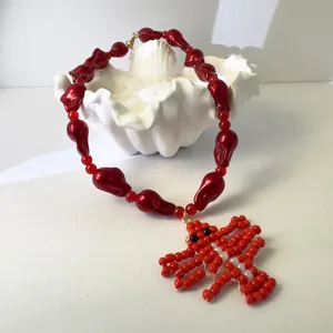 Detail of red lobster pendant necklace with irregular acrylic beads and shell prop.