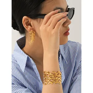 Close-up view of an elegant gold leaf earring and a wide filigree cuff bracelet on a model