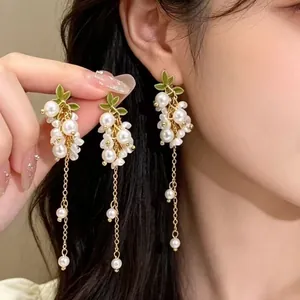 Vue détaillée de boucles d'oreilles en perles blanches avec feuilles et dorures.