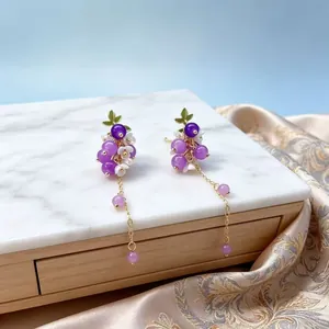 Gros plan de boucles d'oreilles grappes de raisin violettes avec chaînes dorées.