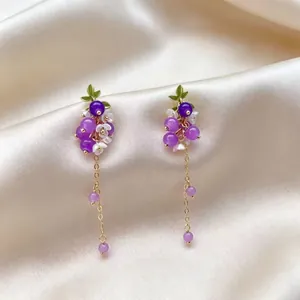 Gros plan de boucles d'oreilles pendantes raisin violet avec chaînes dorées sur soie.