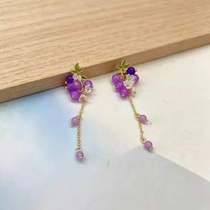 Détail de boucles d'oreilles en forme de raisin violet avec pampilles et fleurs blanches