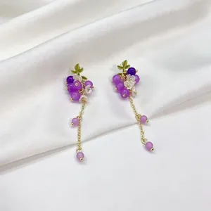 Détail de boucles d'oreilles grappes de raisin violettes avec fleurs et chaînes.
