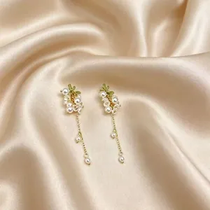 Boucles d'oreilles pendantes dorées avec perles blanches et accents de feuilles vertes.