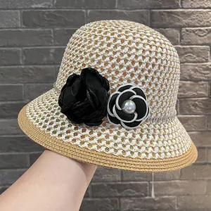 Close-up of elegant woven straw sun hat with black rose and pearl camellia details.