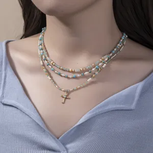 Three-layer beaded necklace with turquoise, pearls, and a gold cross pendant detail