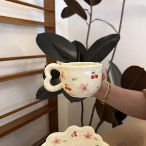 Detail of cream ceramic coffee cup and cloud saucer set with hand-painted cherry patterns