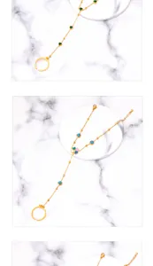 Detail of gold finger bracelet featuring green heart charms and clover patterns on marble