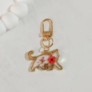 Detail view of cat-shaped gold metal keychain with red dried flowers in clear resin
