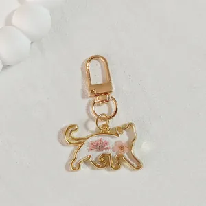 Close-up of golden cat keychain pendant with delicate pink dried flowers inside