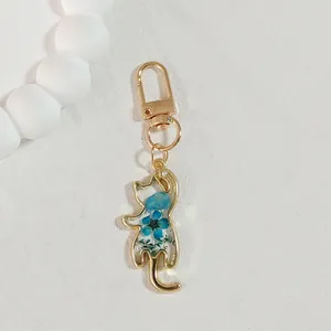 Close-up of a cat-shaped gold keychain filled with blue dried flowers in clear resin