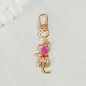 Close-up detail of a cat-shaped resin keychain featuring vibrant pink dried flowers