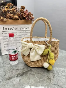 Hand-woven straw handbag featuring a white satin bow and colorful crochet fruit charm