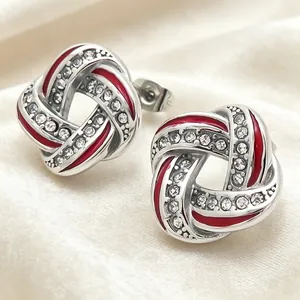 Close-up of silver-tone knot earrings with red enamel and crystals on white fabric.