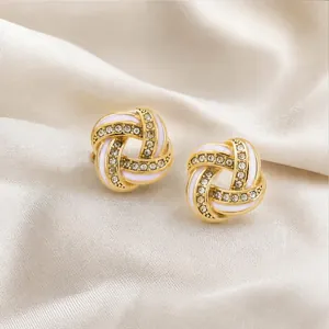 Close-up of elegant gold knotted earrings with white enamel and sparkling crystals
