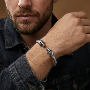 Close-up detail of a men's stainless steel open cuff bracelet with dual skull motifs