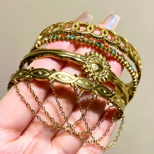 Detail view of multiple gold stainless steel bangles with sun motif and hanging chains.