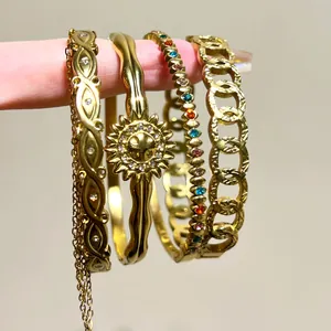 Close-up detail of four gold stainless steel bangles with hollow and gemstone designs