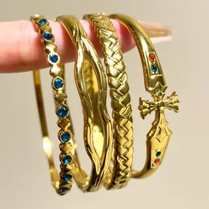 Detailed view of four different gold stainless steel bangles with blue stones and cross charm.
